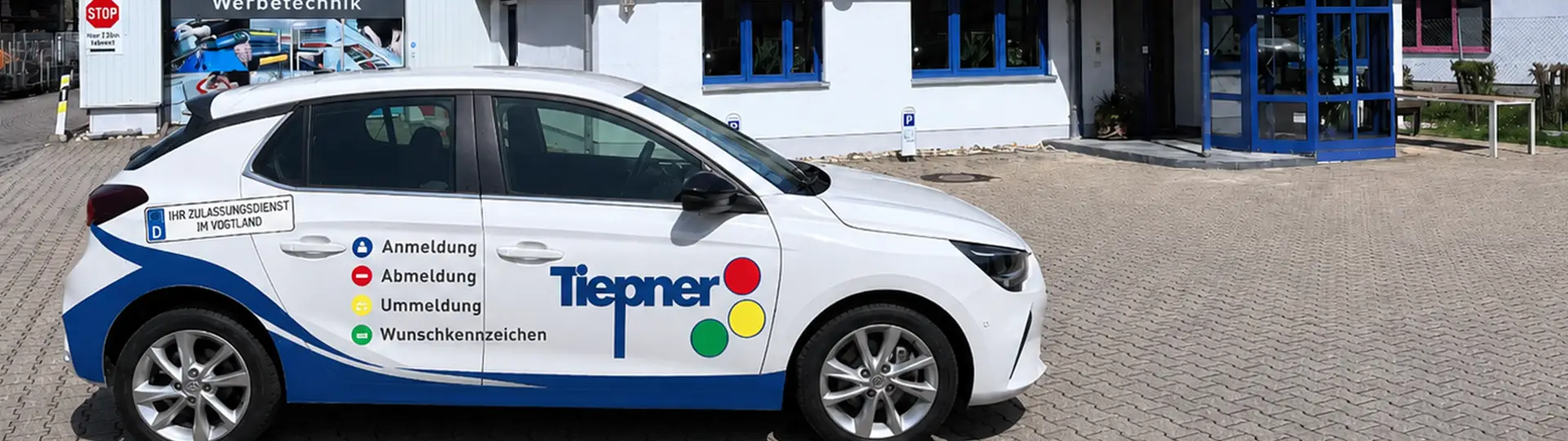 Tiepner Firmengebäude mit beschriftetem Fahrzeug für Zulassungsdienst, Verkehrssicherung und Werbetechnik vor modernem Eingangsbereich.