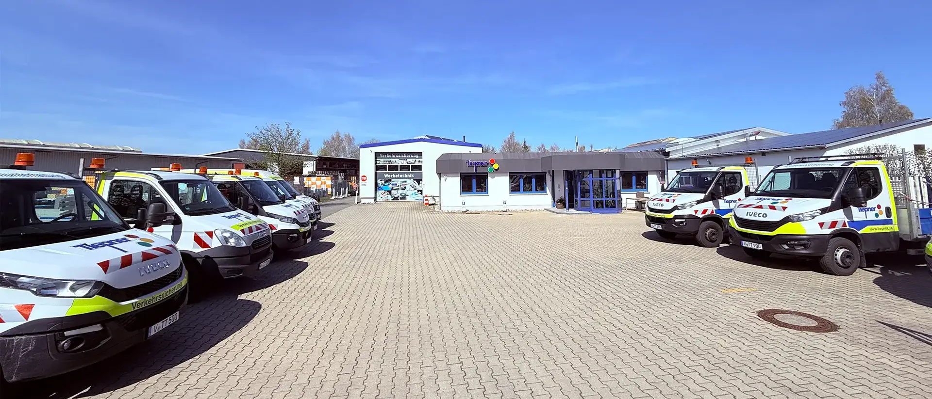 Tiepner Unternehmen mit Fuhrpark für Verkehrssicherung vor Firmengebäude, Werbetechnik-Bereich und modernem Eingangsbereich.